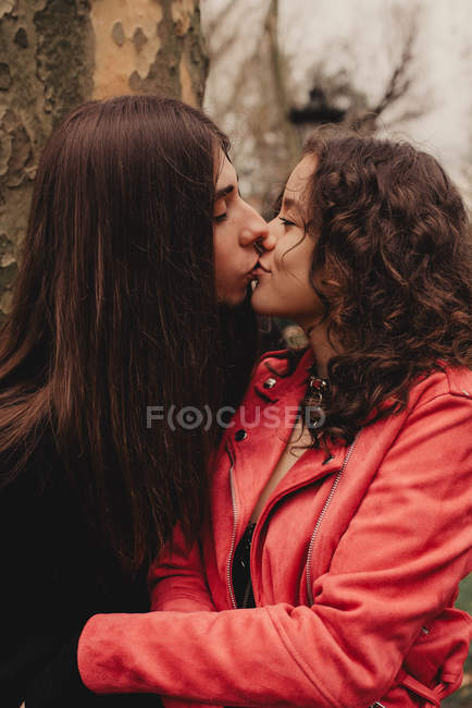 Langhaariger Mann umarmt und küsst Frau neben Baum — Stockfoto