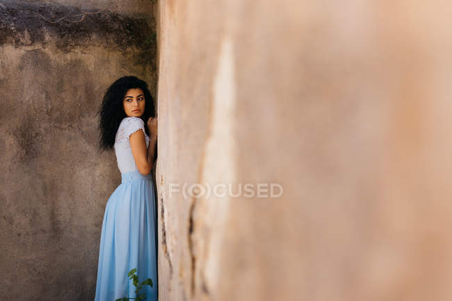 Vista laterale di donna attraente in abito elegante guardando lontano mentre in piedi vicino alla sporca parete grungy — Foto stock