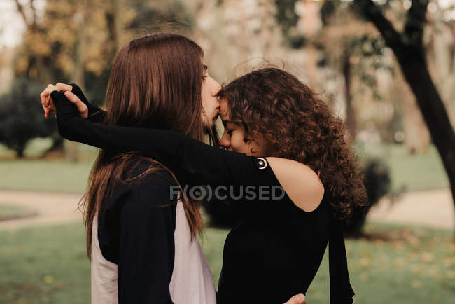 Длинноволосый мужчина обнимает и целует женщину возле дерева — стоковое фото
