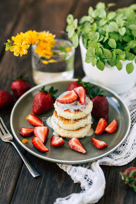 Délicieuses crêpes molles aux fraises fraîches placées sur une assiette en céramique près d'une plante en pot et du verre aux fleurs jaunes — Photo de stock
