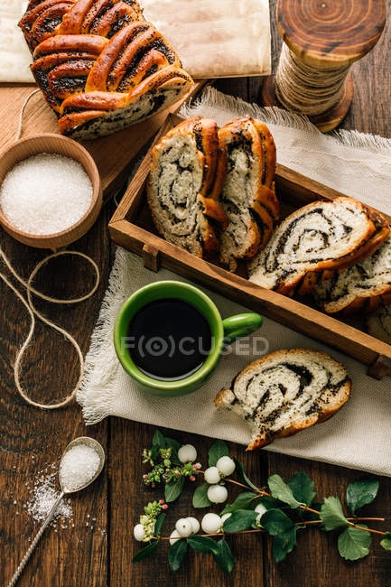 Fresh slices bun with poppy seeds with sugar, coffee and plants on wooden tabletop. — Stock Photo