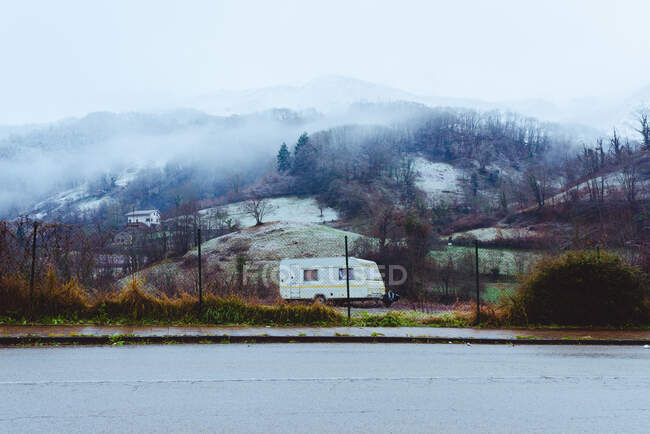 Mobile home parked on countryside road near mountains in fog in rainy weather — Stock Photo