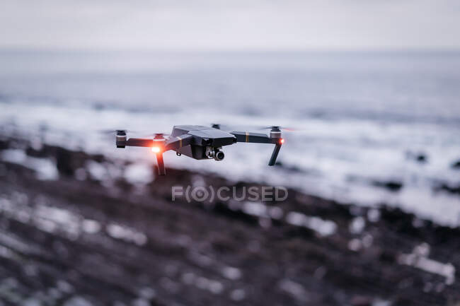 Drone moderno con luces brillantes volando sobre un fondo borroso de mar y costa - foto de stock