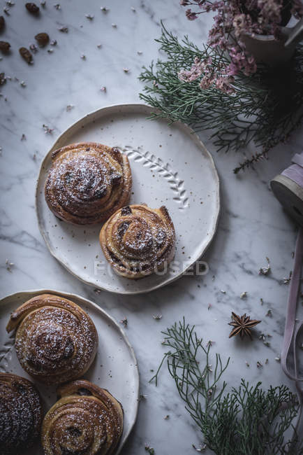 Top view of plates with cinnamon rolls on table decorated with herbs and spices. — Stock Photo