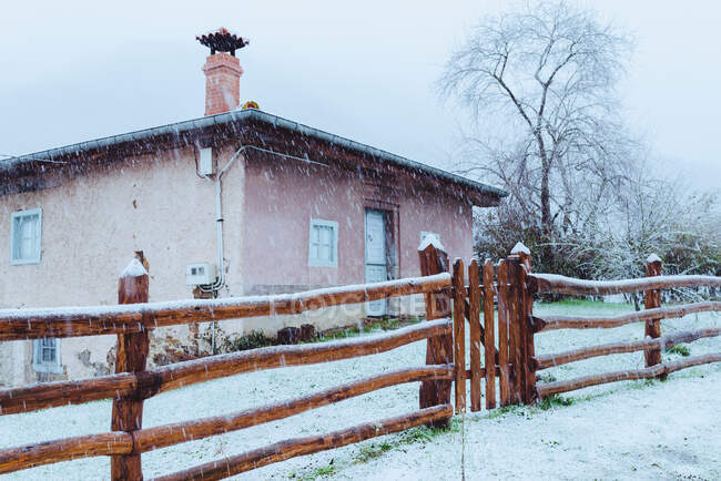 Facciata di casa di campagna rosa e recinzione in legno con tempo nevoso — Foto stock