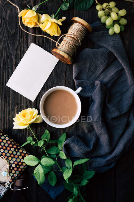 Desde arriba hermosas rosas amarillas y nota en blanco cerca de la taza de café fresco en la mesa de madera . - foto de stock