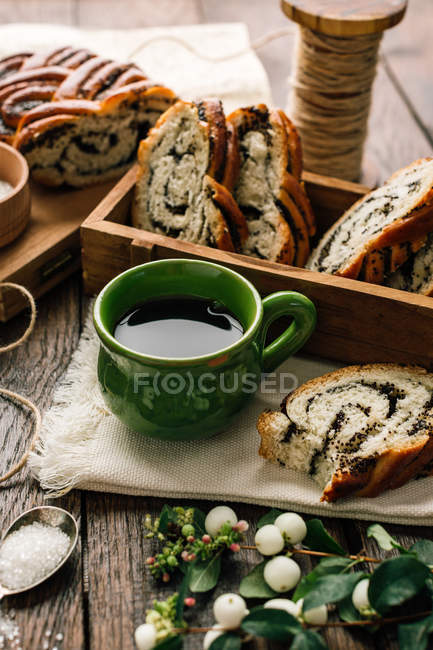 Fresh slices bun with poppy seeds with sugar, coffee and plants on wooden tabletop. — Stock Photo