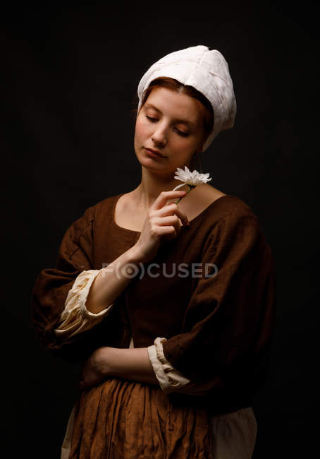 Medieval jovem empregada segurando flor no fundo preto . — Fotografia de Stock