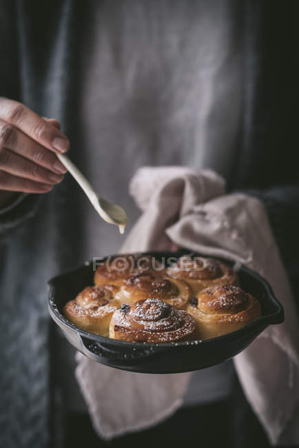 Unrecognizable female with small spoon adding sweet sauce to delicious fresh cinnamon rolls on frying pan — Stock Photo