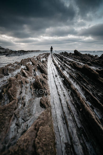 Silhouette of unrecognizable person standing on rough rocky surface near sea on cloudy day — Stock Photo
