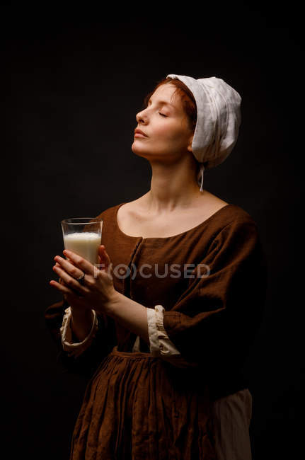 Criada medieval con vaso de leche sobre fondo negro . - foto de stock