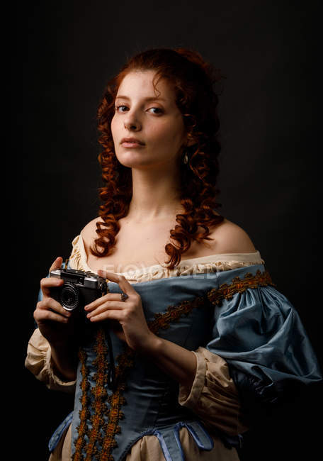 Beautiful female in lovely baroque dress holding photo camera on black background. — Stock Photo