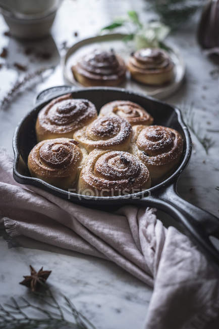 Frying pan with tasty fresh cinnamon rolls placed near napkin on marble tabletop. — Stock Photo