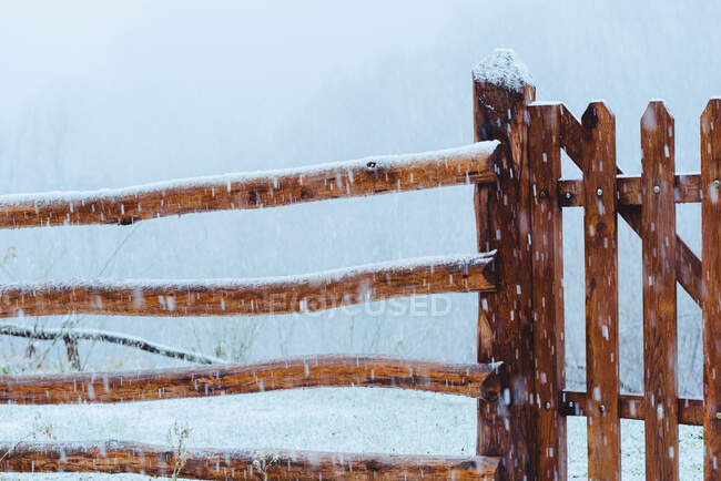 Cerca de madeira velha entre a queda de neve perto da terra na neve no inverno — Fotografia de Stock