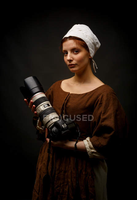 Medieval woman holding modern photo camera on black background. — Stock Photo