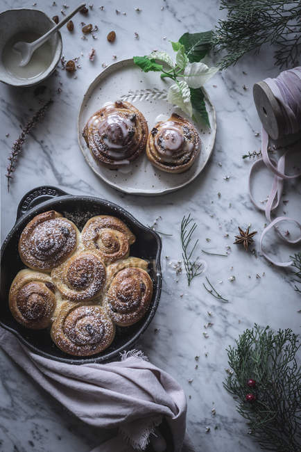 Top view of pan and plate with cinnamon rolls on table decorated with herbs and spices. — Stock Photo