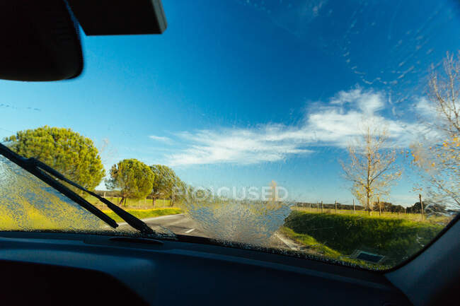 Удивительный вид на асфальтовую сельскую дорогу и величественную природу в солнечный день через чистое лобовое стекло современного автомобиля — стоковое фото