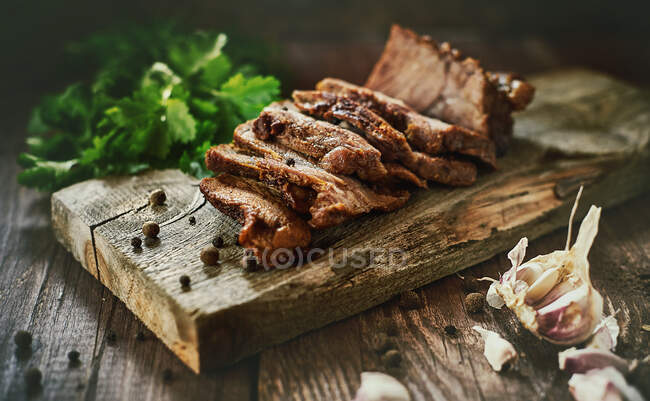 Fresh garlic and parsley lying on timber tabletop near board with slices of yummy baked ham — Stock Photo