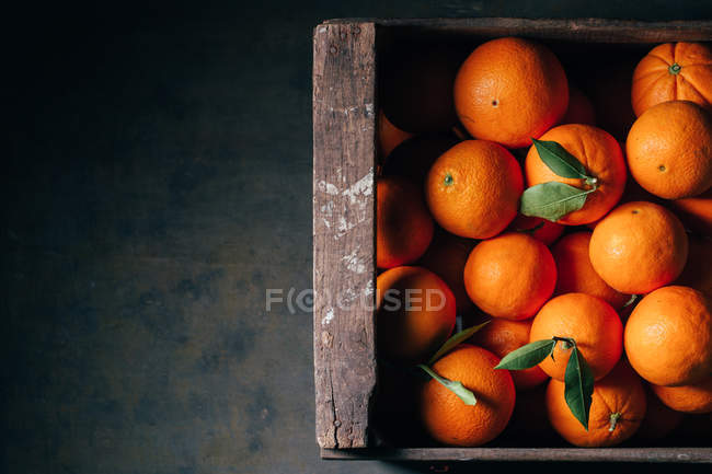 Fresh oranges in old wooden box on dark background — Stock Photo