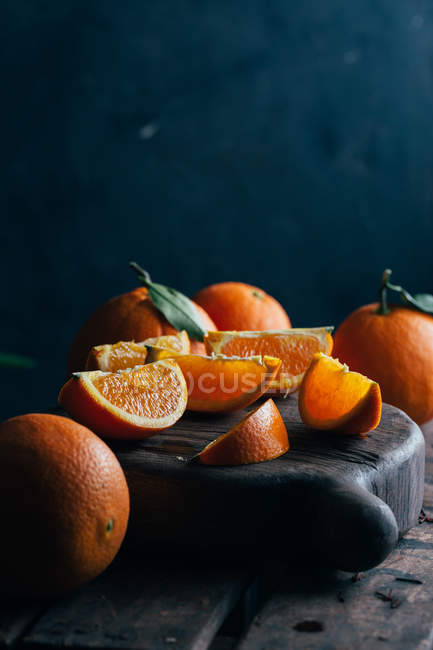 Naranjas frescas enteras y cortadas sobre fondo de madera oscura - foto de stock