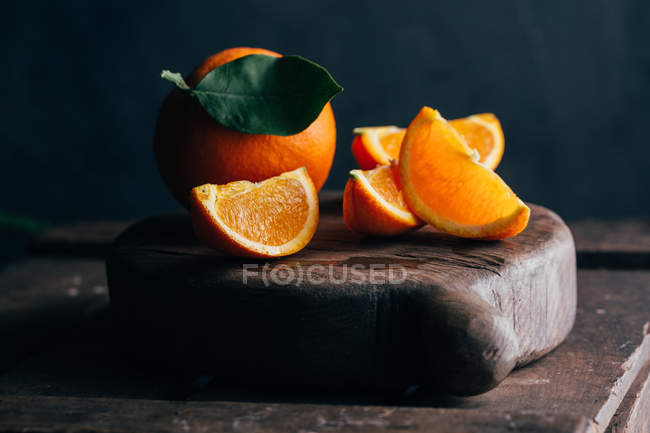 Fresh whole and cut oranges on dark wooden background — Stock Photo