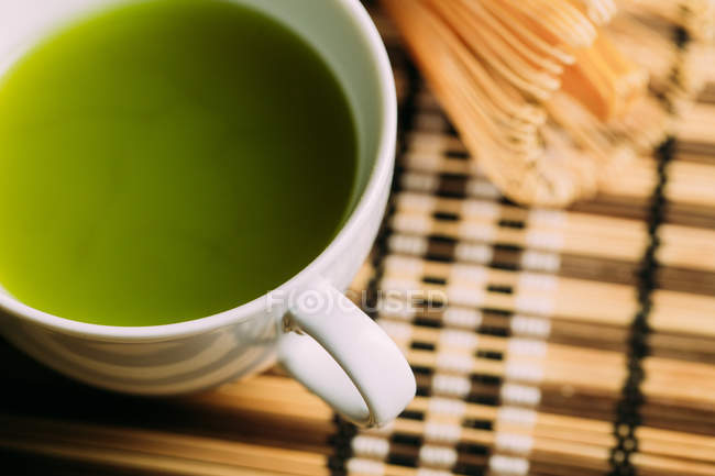 Close-up of cup with fresh green matcha tea and bamboo whisk preparing tool on table. — Stock Photo