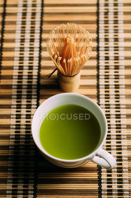 Primo piano di tazza con tè matcha verde fresco e frusta di bambù strumento di preparazione sul tavolo . — Foto stock