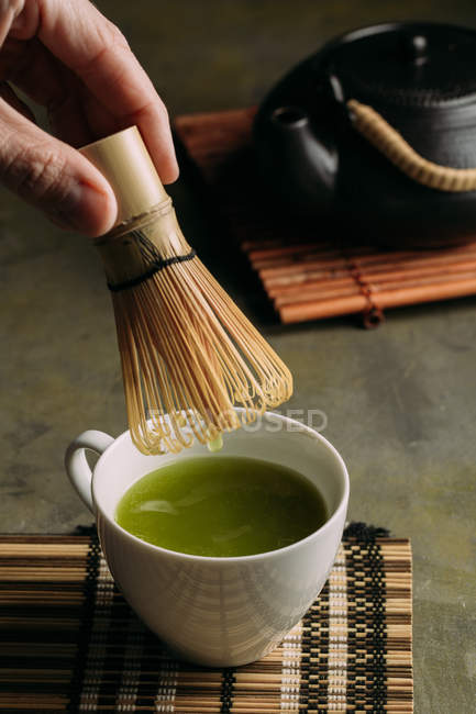 Close-up de mão de pessoa preparando chá matcha com batedor de bambu . — Fotografia de Stock