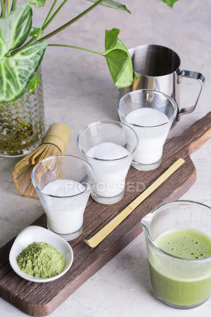 Glasses of milk and matcha powder, process of preparing matcha latte beverage. — Stock Photo