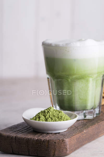 Matcha latte beverage in glass and green matcha powder on wooden board, close-up. — Stock Photo