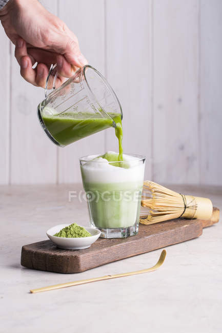 Mão de pessoa derramando chá matcha no leite enquanto prepara a bebida de latte matcha . — Fotografia de Stock