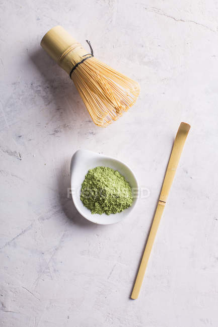 Green matcha tea powder and bamboo whisk with spoon on table. — Stock Photo