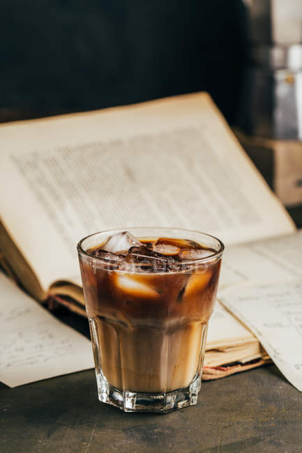 Kalter Espresso-Kaffee im Glasglas auf dunklem Grunge-Hintergrund mit altem Buch — Stockfoto