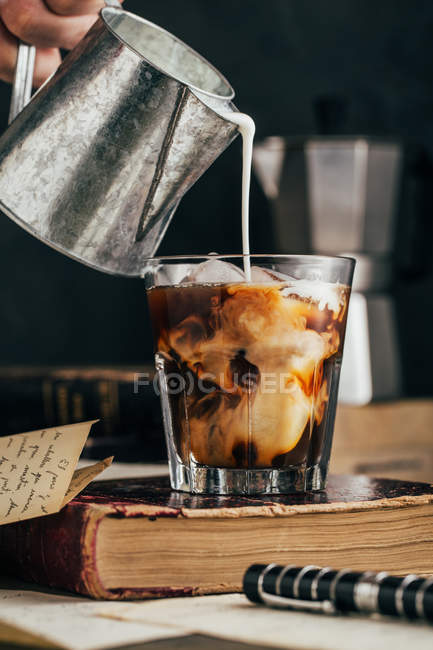 Close-up of human hand pouring milk in cold espresso coffee glass on old old — Stock Photo