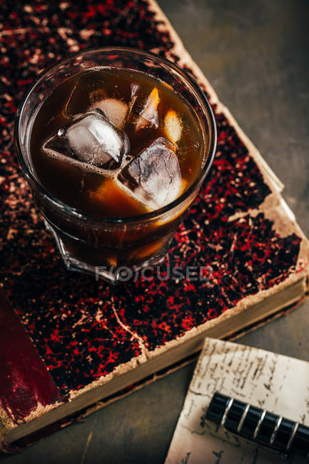 Cold espresso coffee in glass glass on dark grunge background with old book — Stock Photo