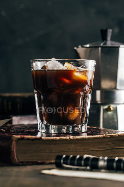 Café espresso frío en vidrio sobre fondo grunge oscuro con libro antiguo - foto de stock
