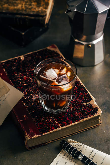 Kalter Espresso-Kaffee im Glasglas auf dunklem Grunge-Hintergrund mit altem Buch — Stockfoto