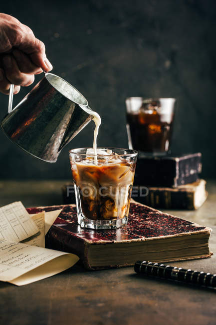 Close-up of human hand pouring milk in cold espresso coffee glass on old old — Stock Photo