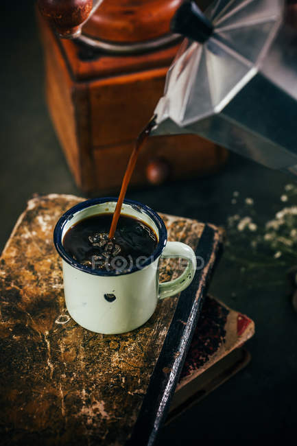 Poring café quente em xícara de esmalte em velhos livros miseráveis — Fotografia de Stock