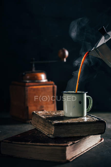 Poring café chaud dans une tasse en émail sur vieux livres minables sur fond sombre — Photo de stock