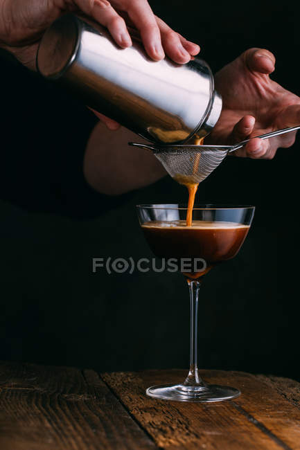 Human hands pouring espresso martini cocktail on dark background — Stock Photo