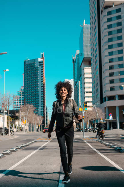 Mujer con pelo afro caminando por las calles de una gran ciudad - foto de stock