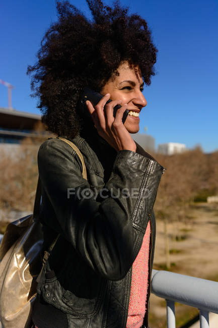 Woman with afro hair looking at her phone while walking on a bridge in a city — Stock Photo