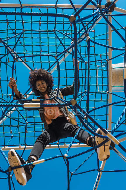 Femme aux cheveux afro grimpant par les attractions pour enfants dans un parc — Photo de stock