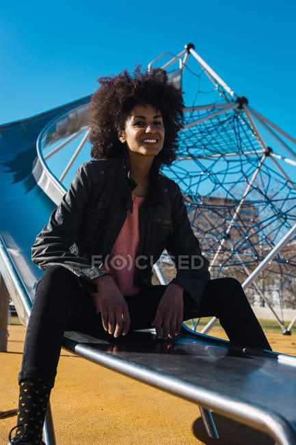 Woman with afro hair jumping down a slide with great joy — Stock Photo
