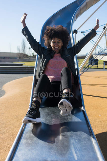 Mujer con el pelo afro saltando por una diapositiva con gran alegría - foto de stock