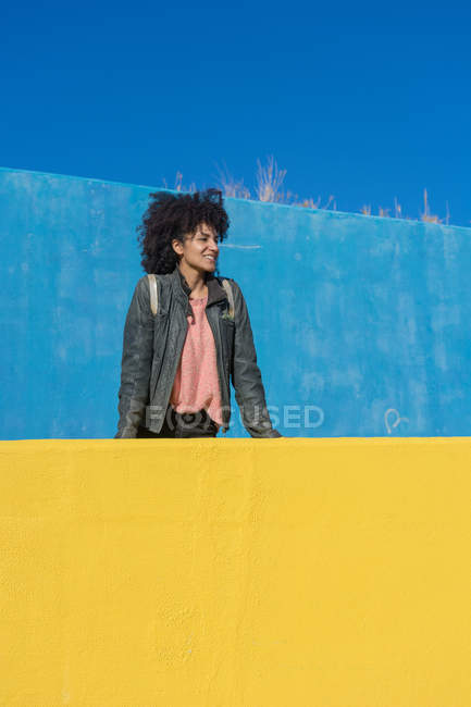 Чорна жінка з волоссям африканського кольору притулилася до яскраво забарвлених стін, дивлячись на свій смартфон і каву. — стокове фото