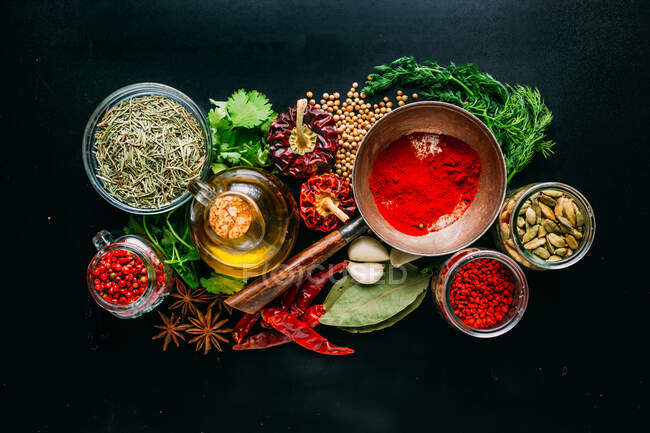 From above set of various spices and herbs placed on black background around bottle of oil — Stock Photo