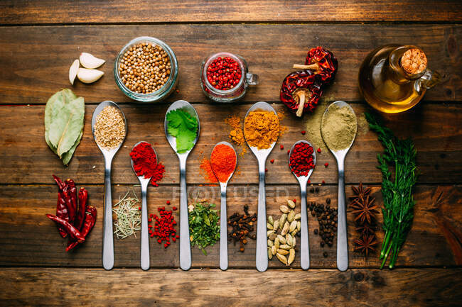Bunch of assorted spices placed in order on lumber tabletop near bottle of oil — Stock Photo