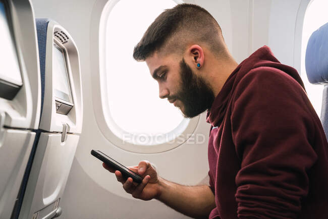 Bearded guy using smartphone in plane — Stock Photo